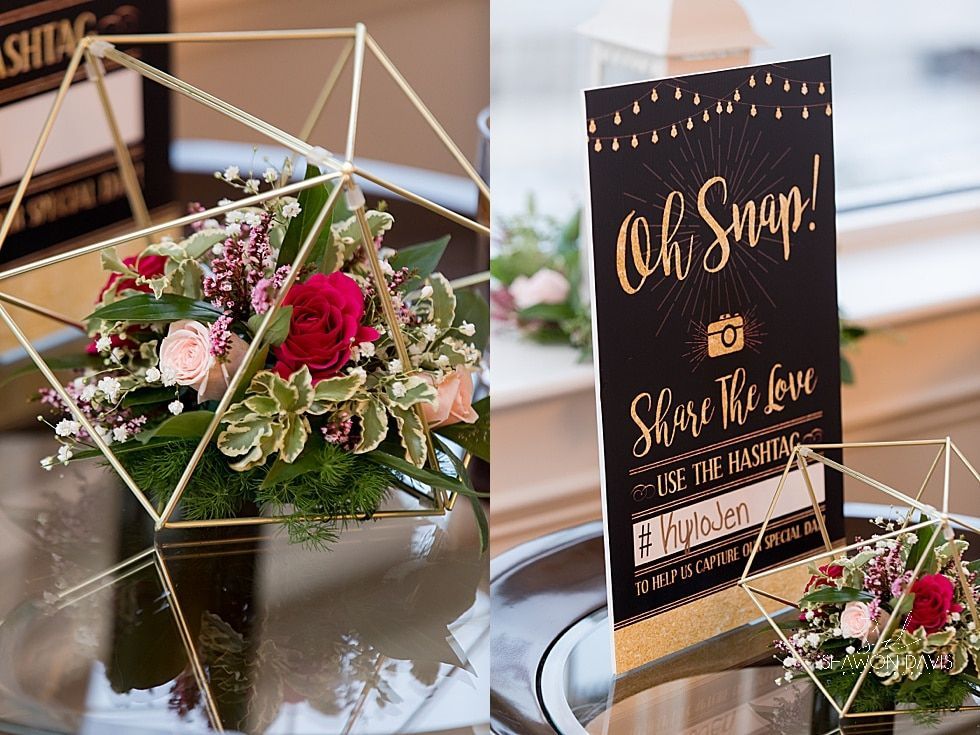 Floral table centerpiece with a black “Oh Snap!” sign and geometric gold decor at a wedding reception
