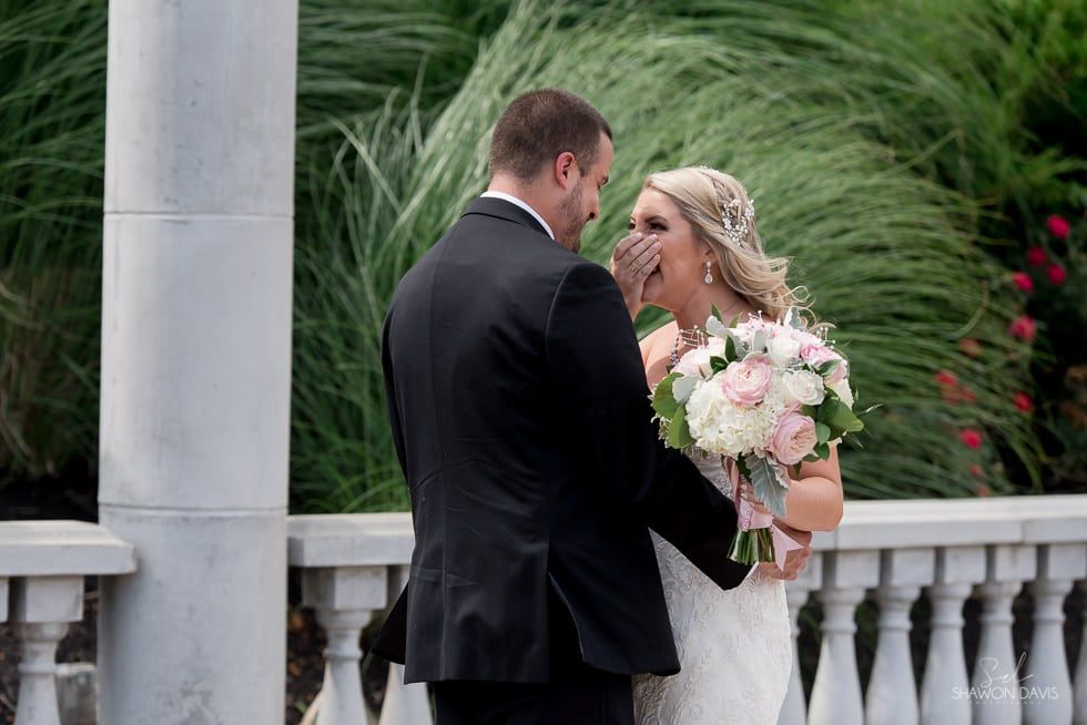 Bride and groom embracing on a balcony, holding a pink and white bouquet.