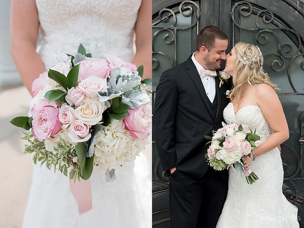 Bride and groom pose in wedding attire beside wrought iron gates, holding pink and white bouquets.