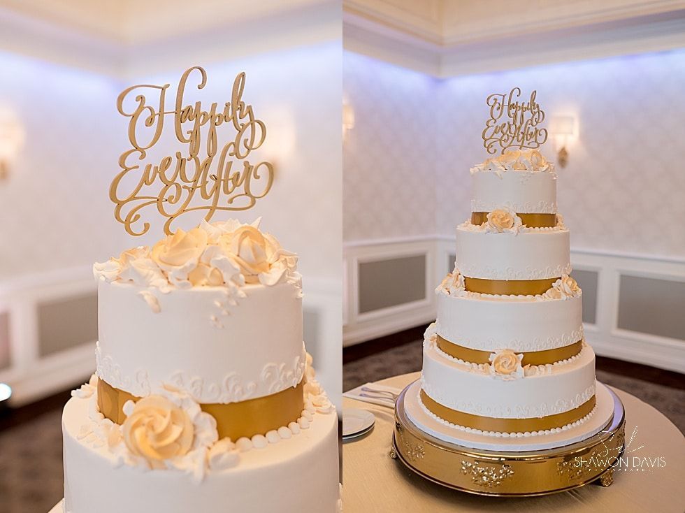 Two elegant white wedding cakes with gold accents on a dessert table in a softly lit room