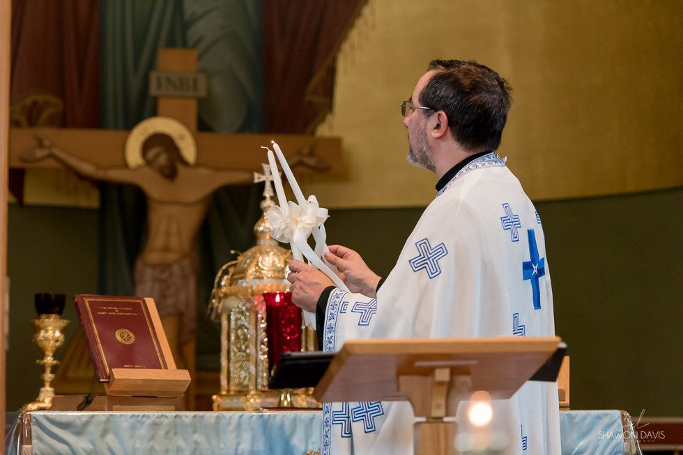 Priest in white vestments at Catholic altar during Mass, facing a crucifix and candles