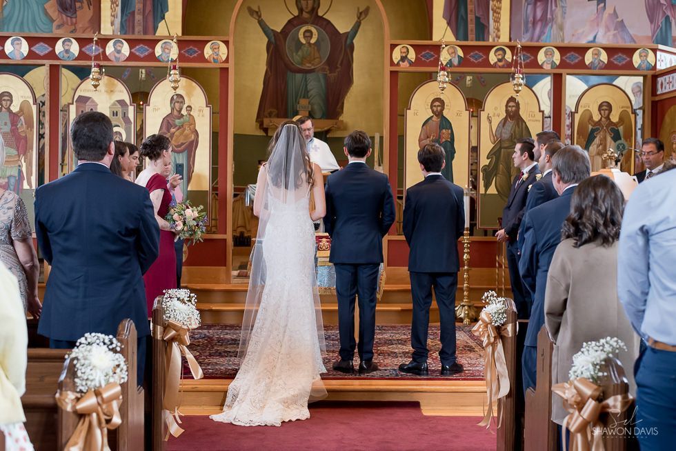 Wedding ceremony in an Orthodox church, with the couple facing the altar and guests standing behind them.