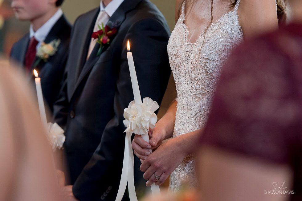 Bride holding a lit candle during a wedding ceremony, with guests seated nearby