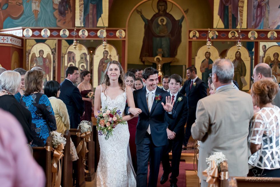 Bride and groom walking down the aisle in a church, guests standing on both sides.