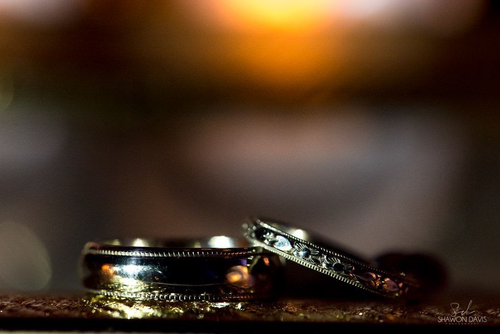 Two wedding rings on a reflective surface with warm blurred lights in the background