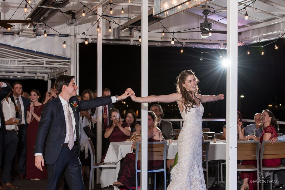 Bride and groom holding hands and spinning under string lights at a wedding reception