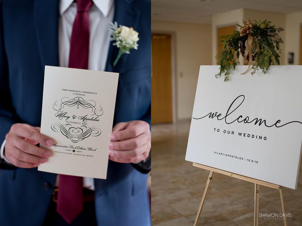 Man in blue suit holding wedding invitation next to a white welcome sign in a hallway