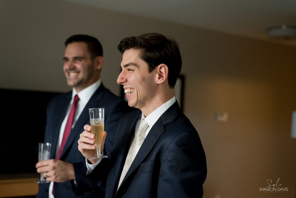 Two men in suits smiling and holding champagne glasses at an indoor event
