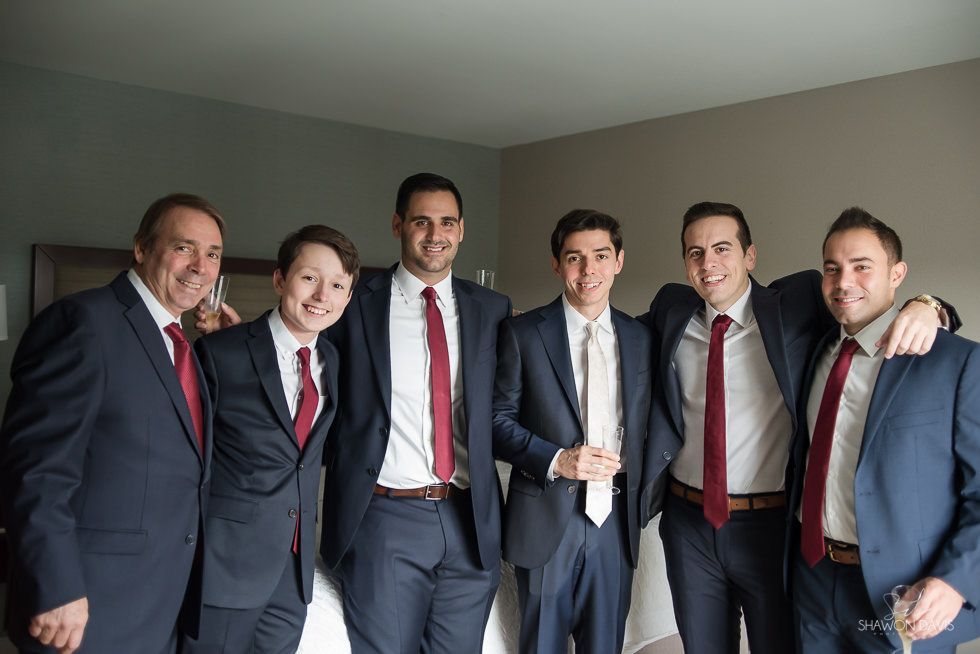 Six men in suits and red ties standing together indoors, smiling at the camera.