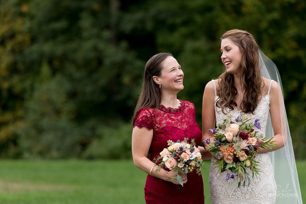 Two women in formal dresses smiling and holding bouquets outdoors on a grassy lawn
