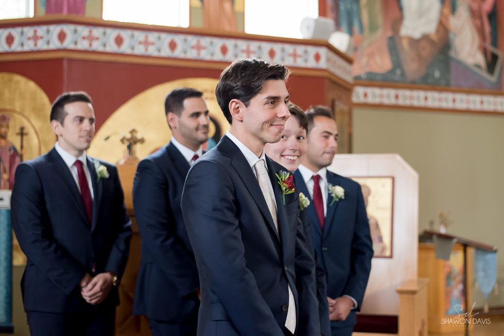 Men in dark suits standing at the altar in a church, one smiling in profile.