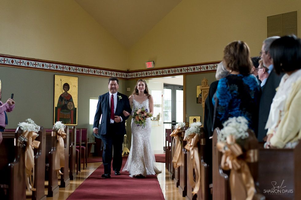 Bride and groom walking down church aisle after their wedding ceremony, guests seated on both sides.