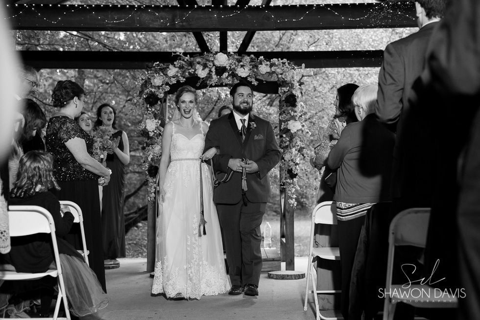 Bride and groom walking down aisle at an outdoor wedding ceremony, guests applauding