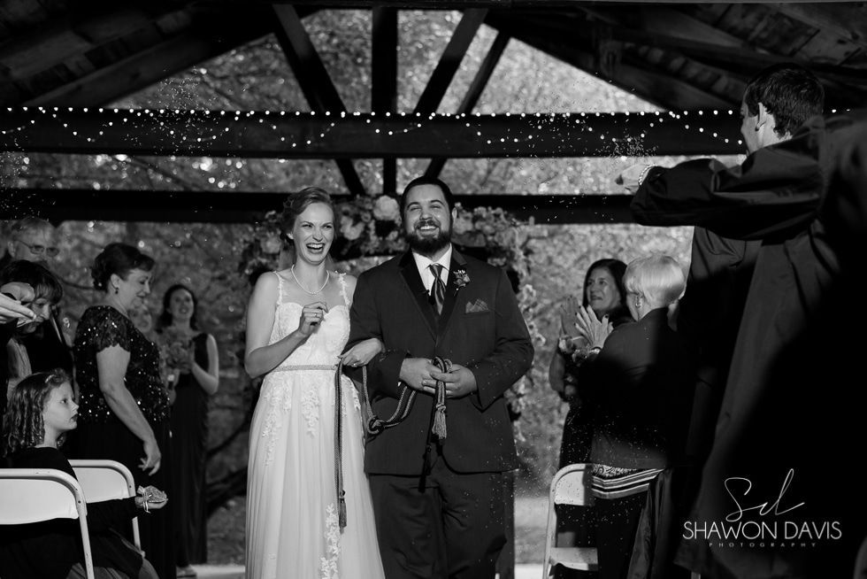 Bride and groom stand at the altar as guests watch, with a musician performing on the right.