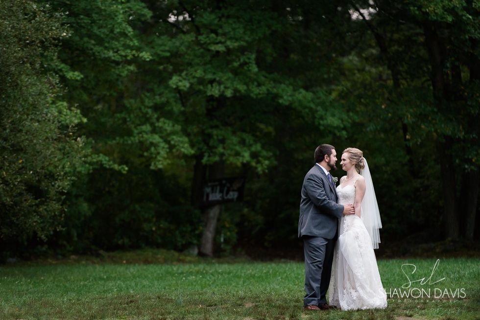 Bride and groom standing in a grassy park, holding hands beneath dark green trees