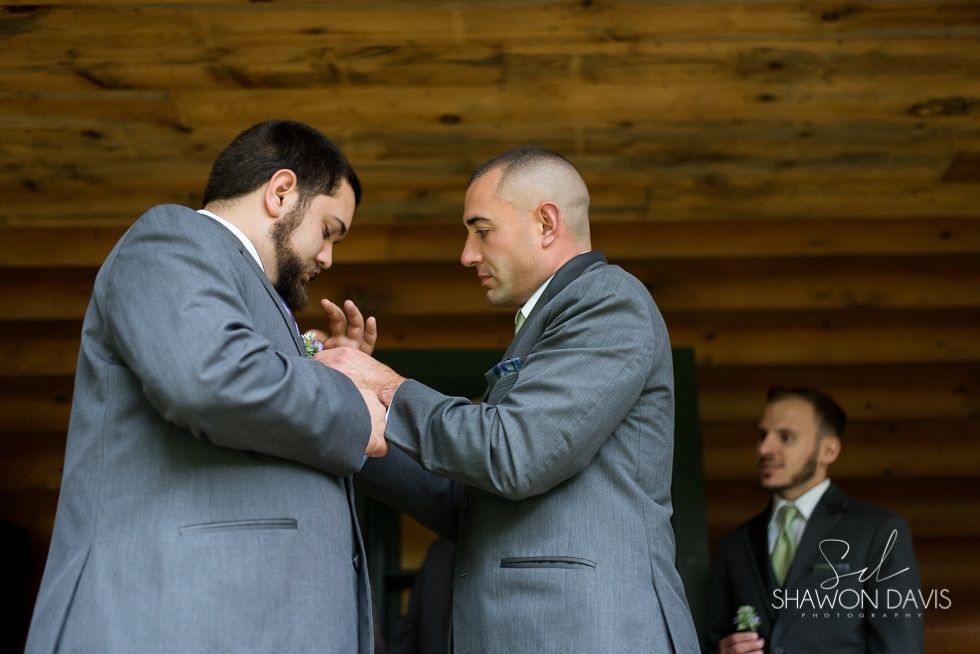 Two men in gray suits holding hands during an emotional ceremony, with a suited man in the background.