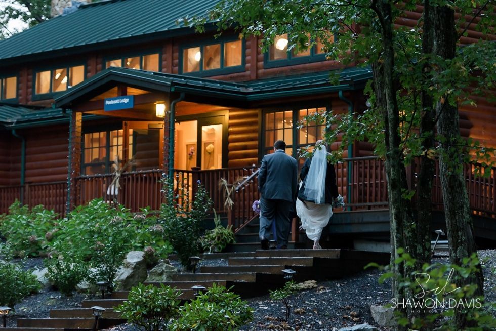 Couple walking up steps to a warmly lit brick house at dusk, surrounded by greenery