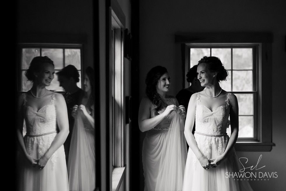 Bride standing in a doorway, smiling with a reflection in the mirror, in a black-and-white portrait