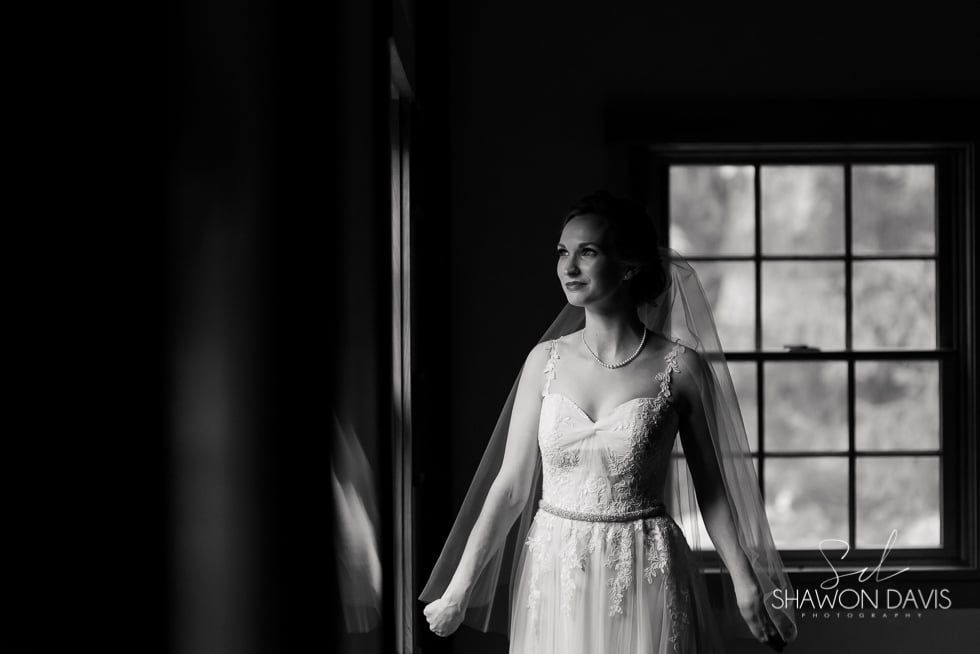 Woman in a white dress standing by a window in soft black-and-white light