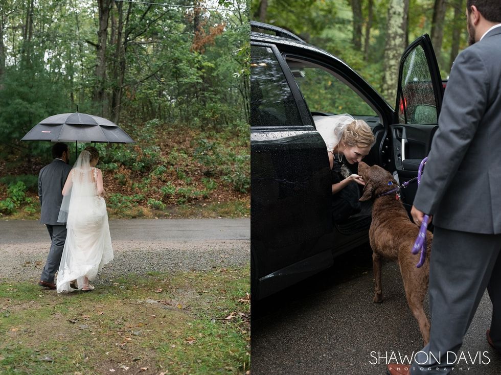 Bride in white under black umbrella with companion beside a car in a wooded area