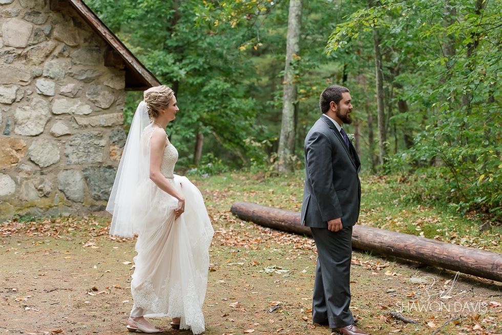 Bride and groom standing outdoors near a stone wall in a wooded area