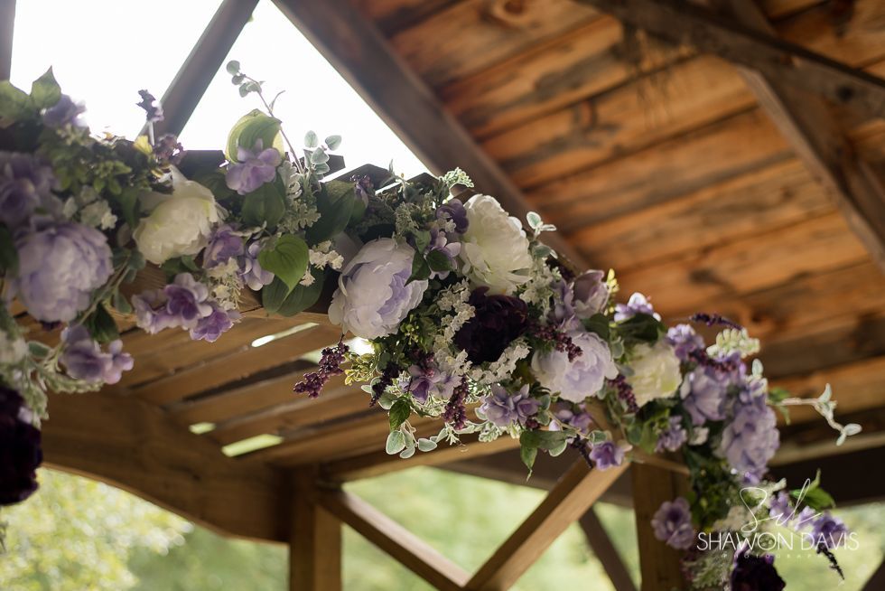Purple and white floral garland hanging from a wooden gazebo ceiling