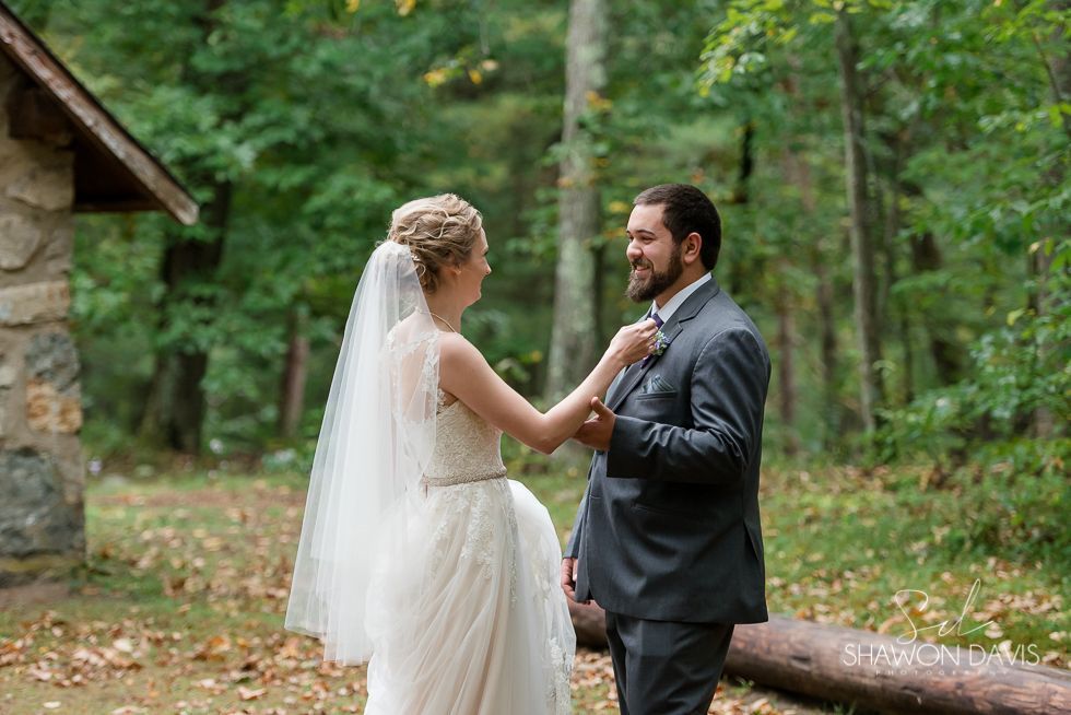 Bride and groom smiling outdoors in a forest, holding hands in wedding attire