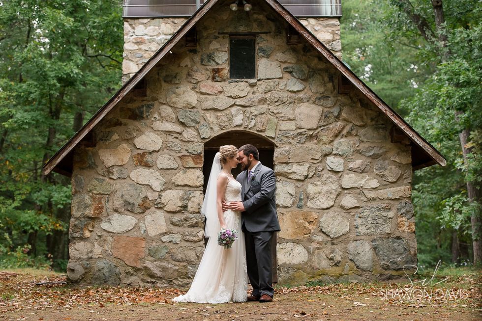 Bride and groom kissing in front of a rustic stone chapel in the woods