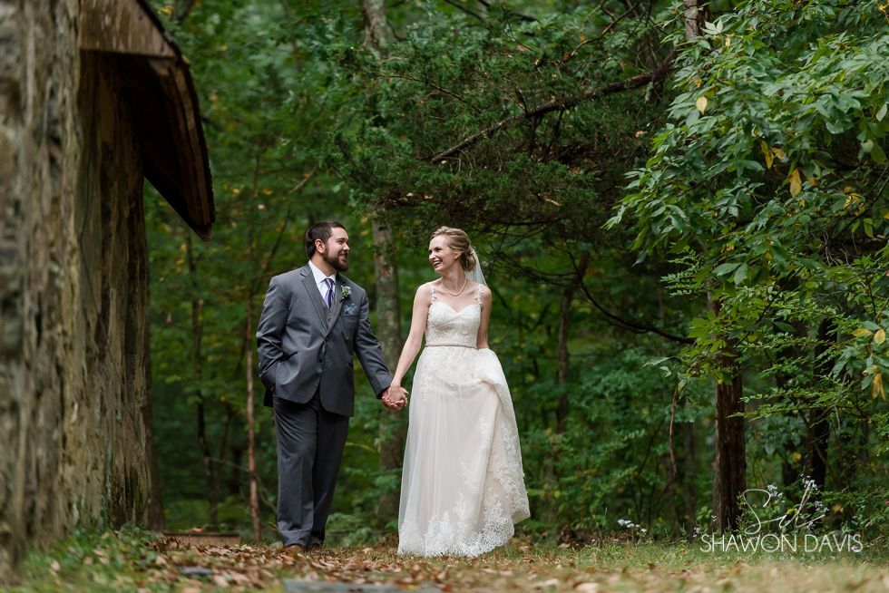 Bride and groom holding hands in a wooded garden beside a rustic building