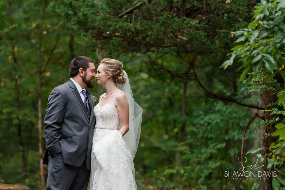 Bride and groom in wedding attire standing close in a green wooded setting