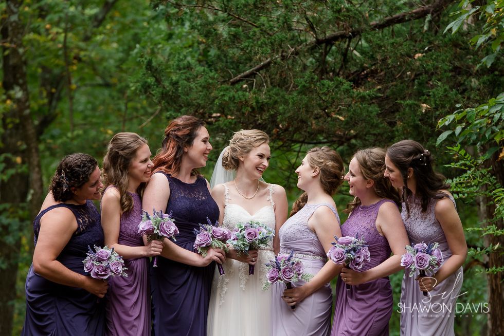 Bride and bridesmaids in purple dresses holding bouquets in a wooded outdoor setting