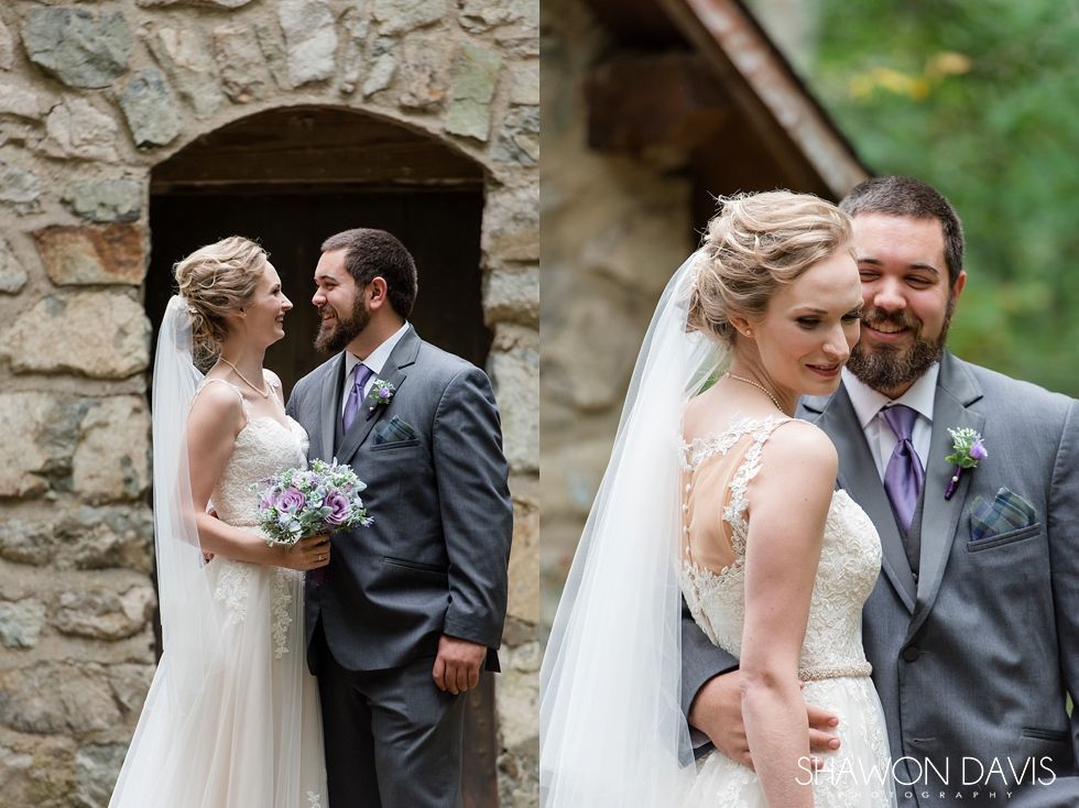 Two brides and two grooms pose in wedding attire outside a stone building, holding bouquets and smiling.