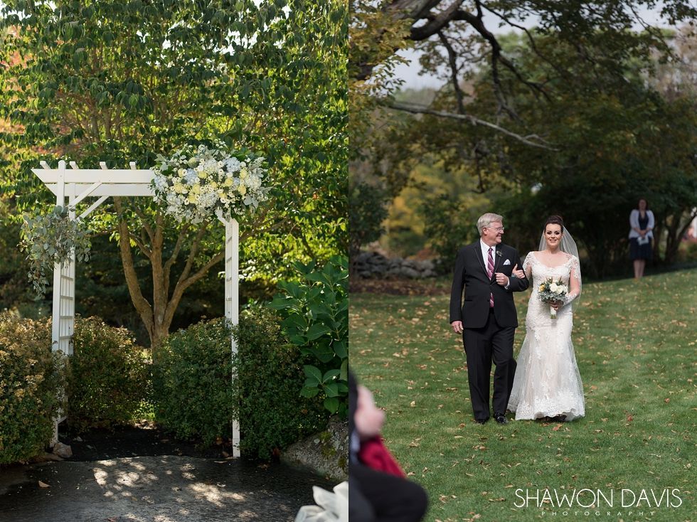 Bride and man in tuxedo walking down a grassy aisle under a white arbor in a garden ceremony