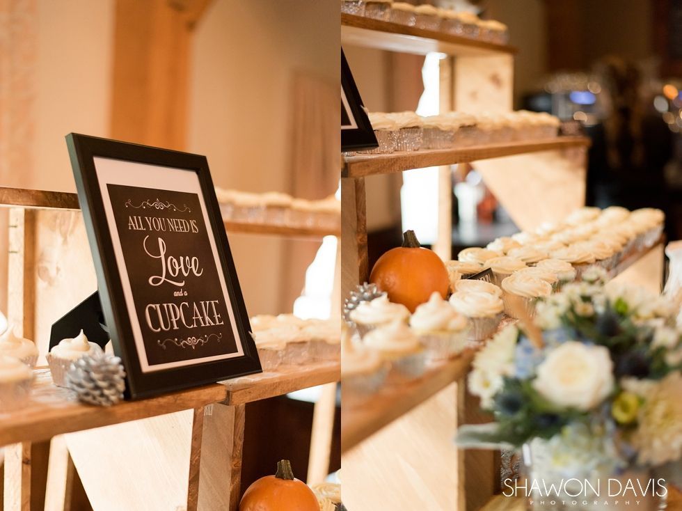 Decorative dessert display with a “Love Cupcake” sign, white flowers, and small pumpkins on rustic shelves