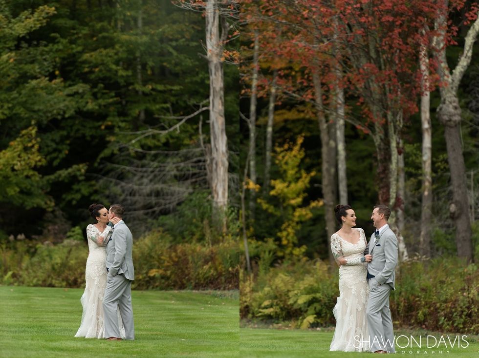 Two couples in white outfits embrace on a grassy lawn beside autumn trees.