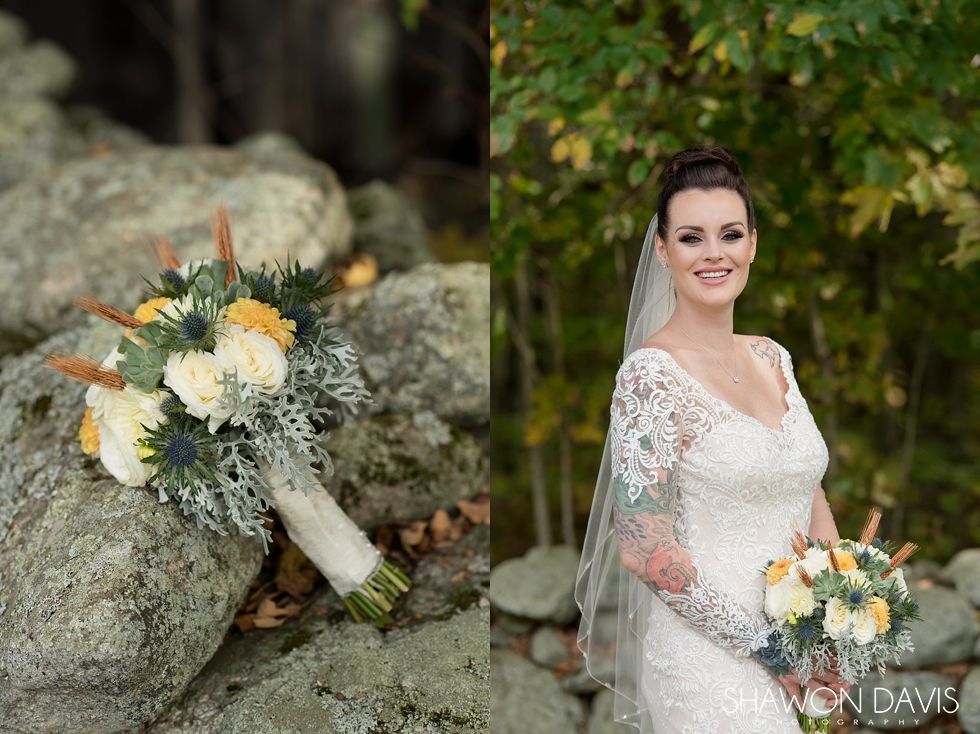 Bride in a white lace gown holding a bouquet beside a rock wall outdoors