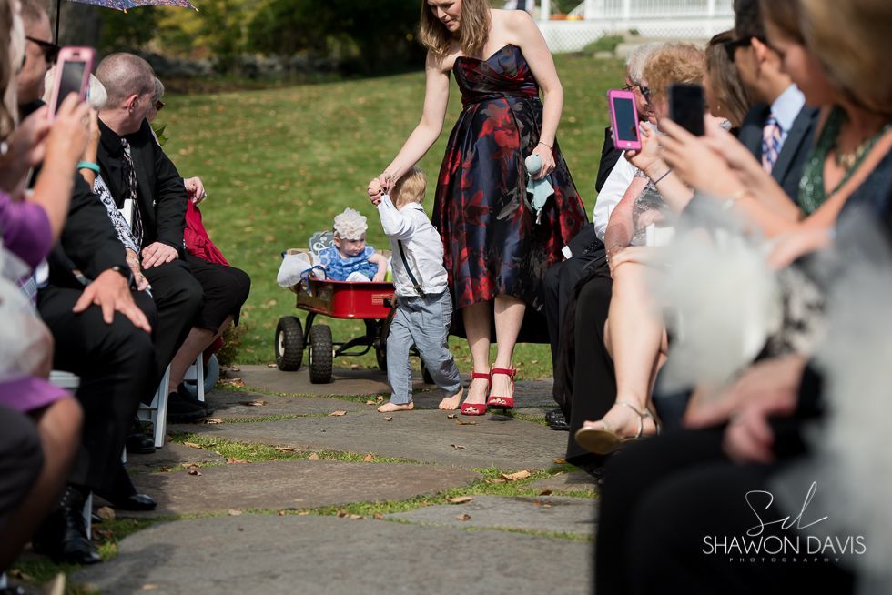 Woman in a black-and-red dress pulling a red wagon down an aisle at an outdoor event