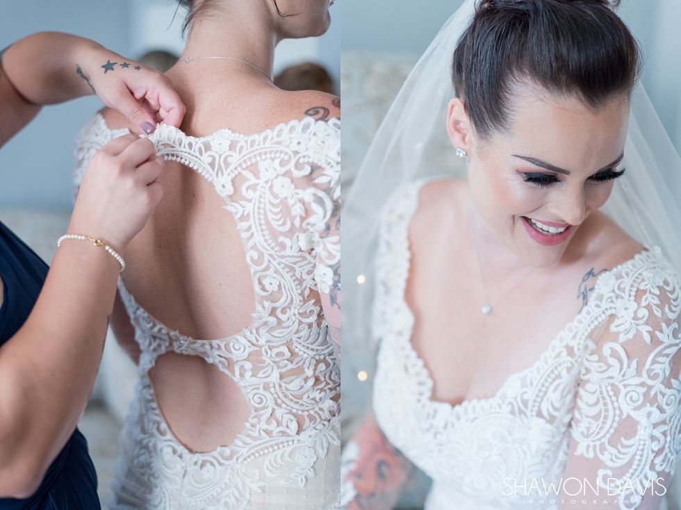 Bridal gown being fastened by hand, with a smiling woman in a white lace dress and veil.
