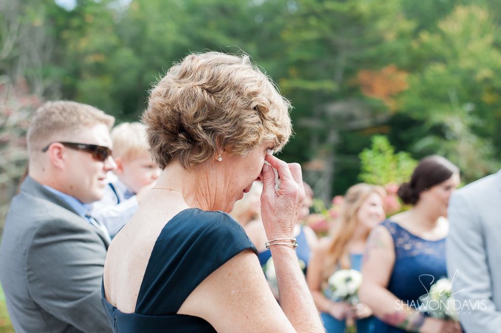Mourning guests seated outdoors at a memorial, one person wiping away tears