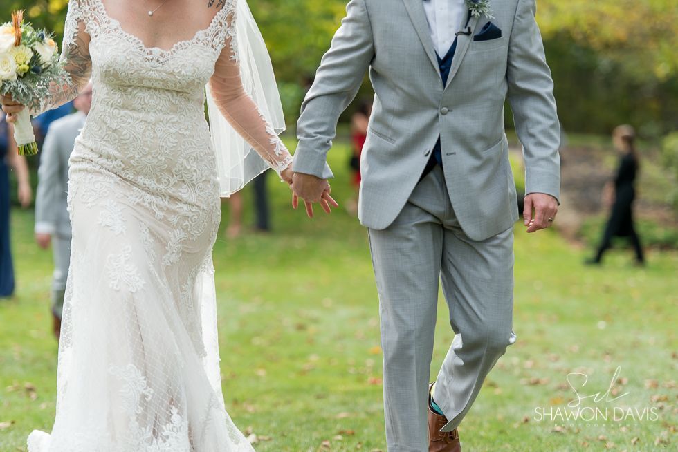 Bride and groom in white dress and gray suit walking hand in hand on a grassy outdoor path