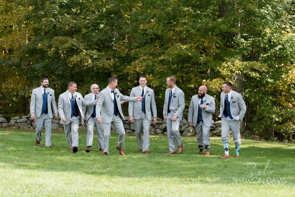 Eight people in gray suits walking across a grassy lawn in front of trees.