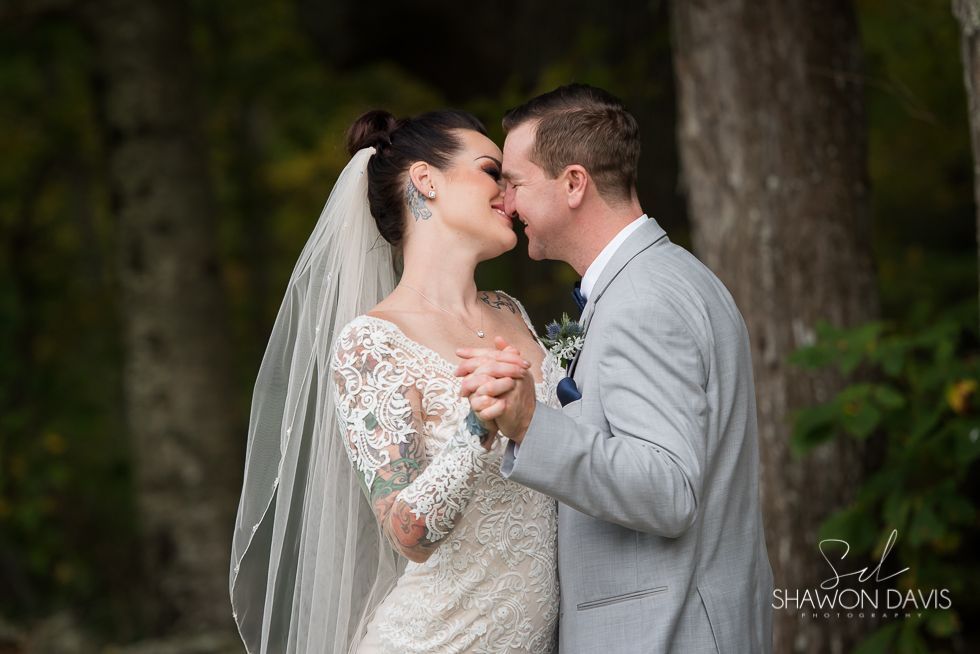 Bride and groom kissing outdoors, bride in white lace dress and veil, groom in gray suit