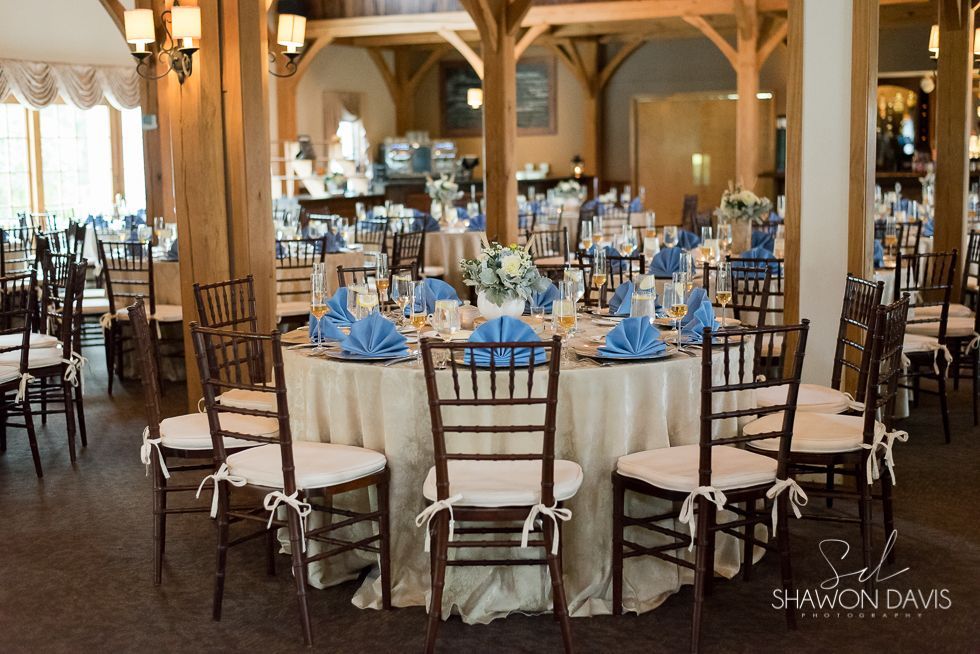 Round banquet tables set for an event in a warmly lit dining hall, with wooden chairs and blue napkins