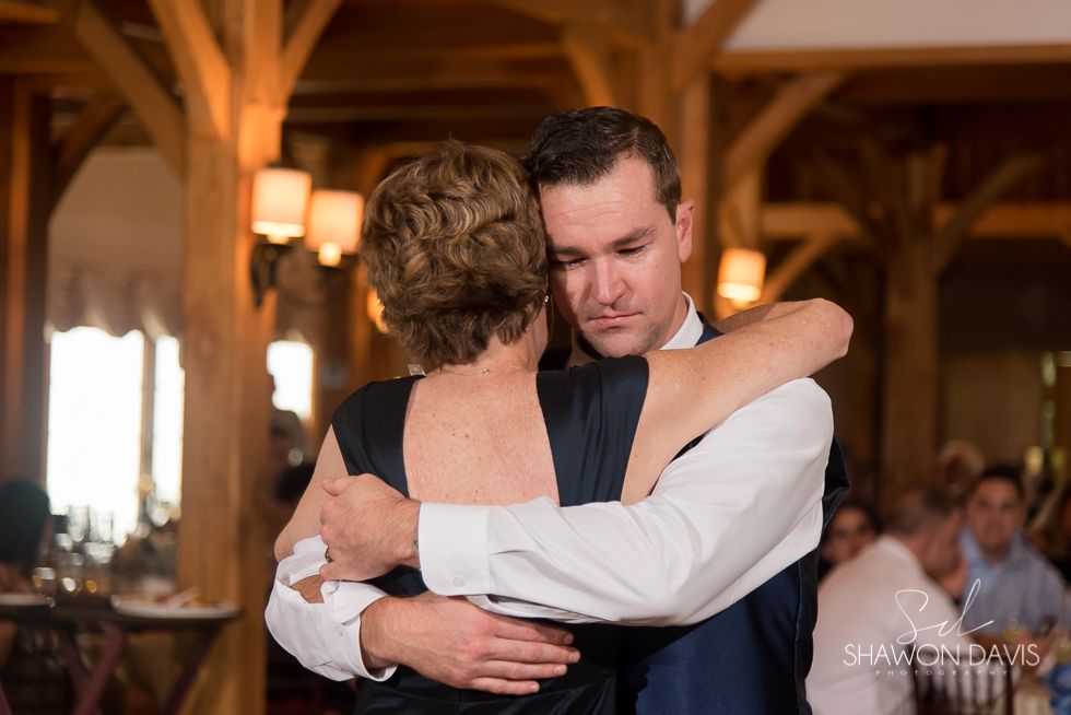 A couple embracing closely during a dance in a warmly lit wooden hall.