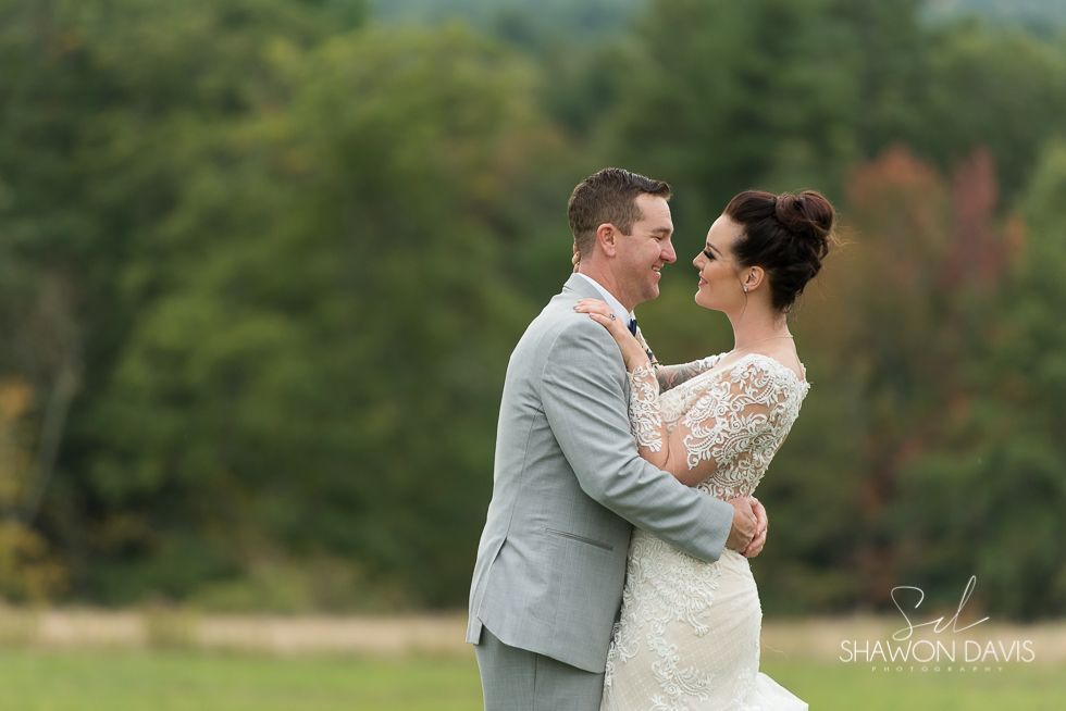 Bride and groom embracing outdoors in a green field, smiling at each other.