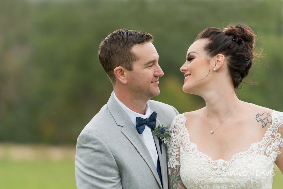 Bride and groom smiling at each other outdoors, with soft green background