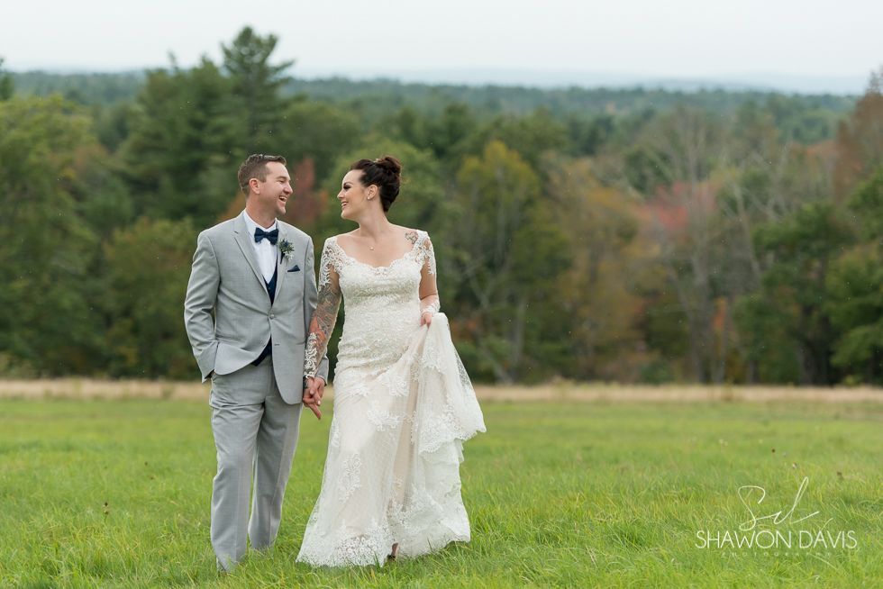 Bride and groom walking hand in hand through a grassy field, with a forest backdrop