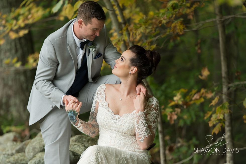 Bride in white gown and groom in light suit holding hands outdoors, smiling at each other.