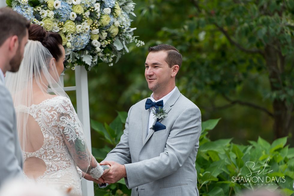 Bride and groom holding hands during an outdoor wedding ceremony under blue and white flowers