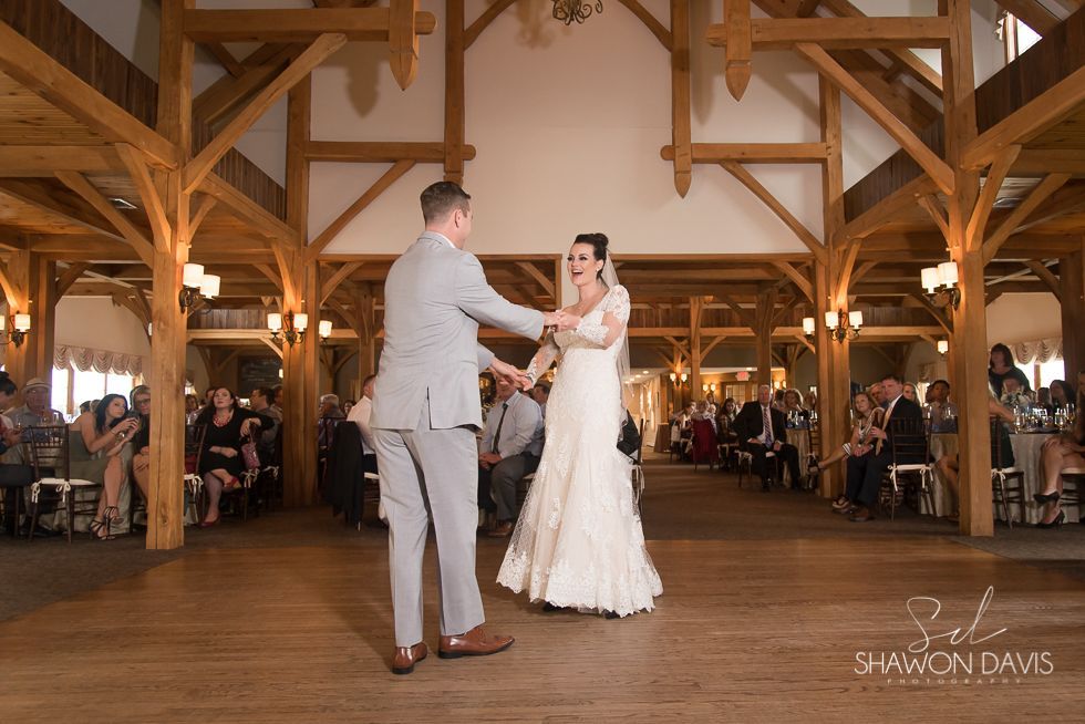 Bride and groom dancing in a rustic wooden reception hall surrounded by seated guests.